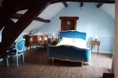 Chambre mansardée avec poutres apparentes, trois lits, une table et des chaises, éclairée par une fenêtre de toit.