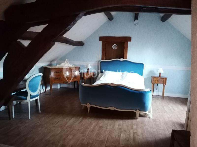 Chambre mansardée avec lit ancien bleu, meubles en bois, parquet et poutres apparentes.