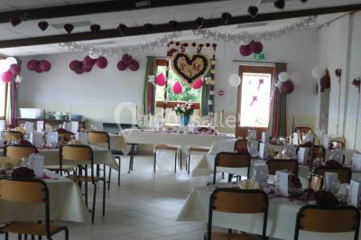 Chambre mansardée avec poutres apparentes, trois lits, une table et des chaises, éclairée par une fenêtre de toit.