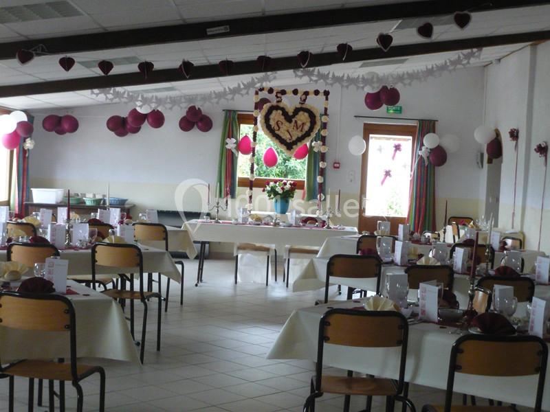 Salle décorée pour un mariage avec tables dressées, guirlandes, ballons et une décoration murale en forme de cœur.