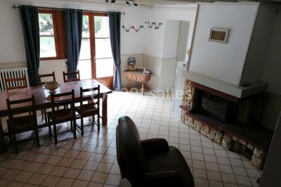 Chambre mansardée avec poutres apparentes, trois lits, une table et des chaises, éclairée par une fenêtre de toit.