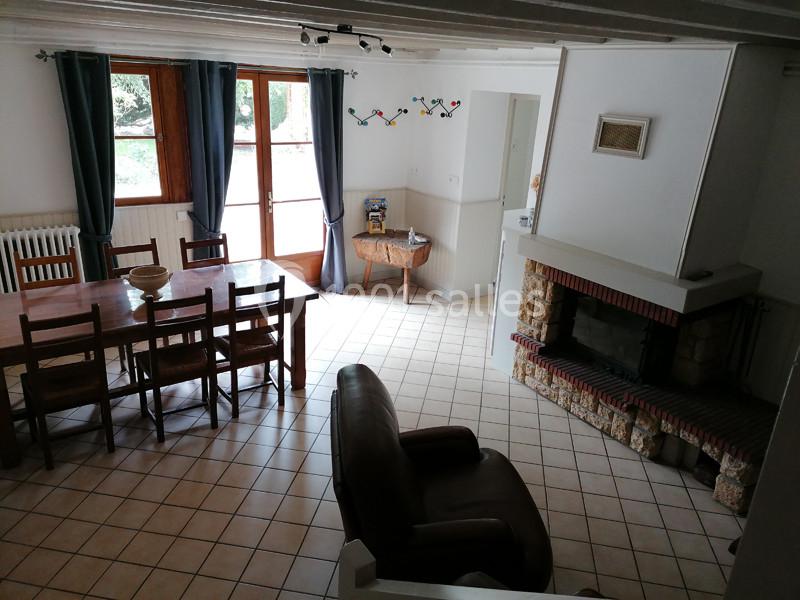 Salle à manger lumineuse avec table en bois, cheminée en pierre, fauteuil en cuir et grandes fenêtres donnant sur l…