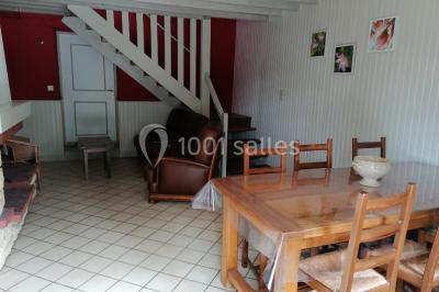 Chambre mansardée avec poutres apparentes, trois lits, une table et des chaises, éclairée par une fenêtre de toit.