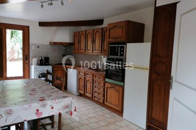 Chambre mansardée avec poutres apparentes, trois lits, une table et des chaises, éclairée par une fenêtre de toit.