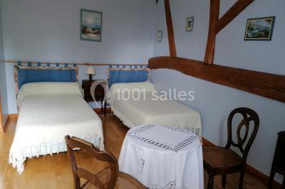 Chambre mansardée avec poutres apparentes, trois lits, une table et des chaises, éclairée par une fenêtre de toit.