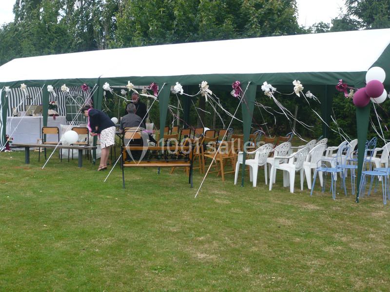 Tente de réception installée dans un jardin avec des chaises, des décorations et des personnes en train de préparer.