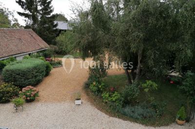 Chambre mansardée avec poutres apparentes, trois lits, une table et des chaises, éclairée par une fenêtre de toit.