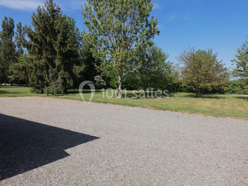 Allée en gravier bordée d'arbres et d'une pelouse sous un ciel bleu dégagé.