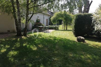 Chambre mansardée avec poutres apparentes, trois lits, une table et des chaises, éclairée par une fenêtre de toit.