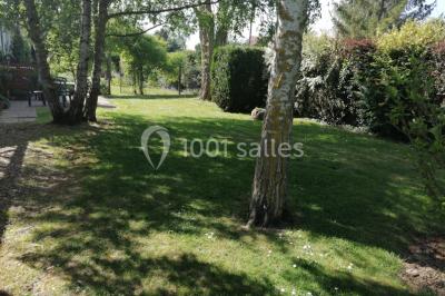 Chambre mansardée avec poutres apparentes, trois lits, une table et des chaises, éclairée par une fenêtre de toit.