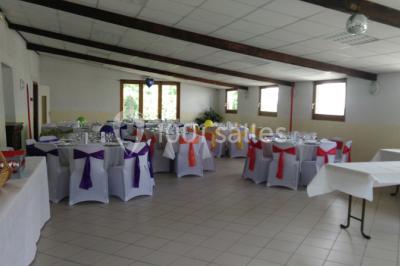 Chambre mansardée avec poutres apparentes, trois lits, une table et des chaises, éclairée par une fenêtre de toit.