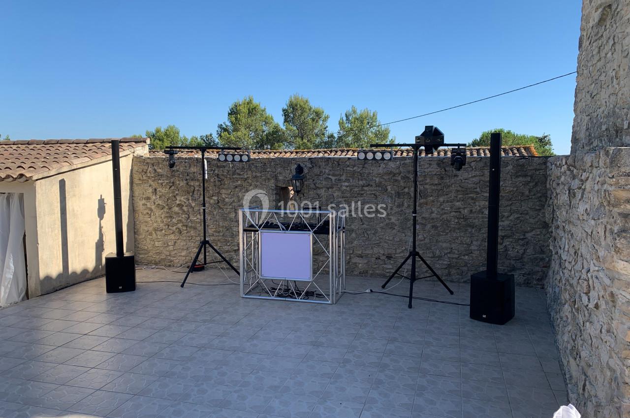 Installation de matériel de sonorisation et d'éclairage en extérieur, sur une terrasse en pierre entourée de murs en pierre.