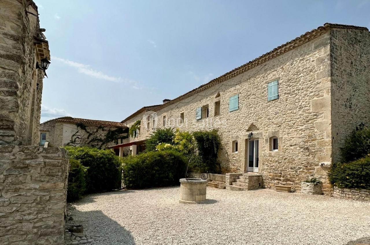 Cour d'une bâtisse en pierre avec puits central, entourée de végétation et éclairée par un ciel dégagé.