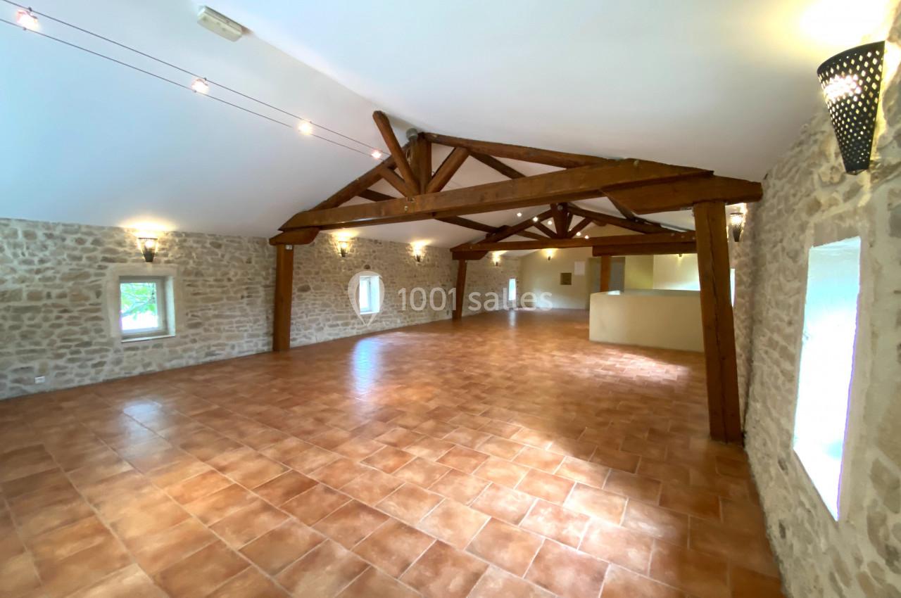 Salle spacieuse avec poutres en bois apparentes, murs en pierre et sol en carrelage, éclairée par des fenêtres et des…