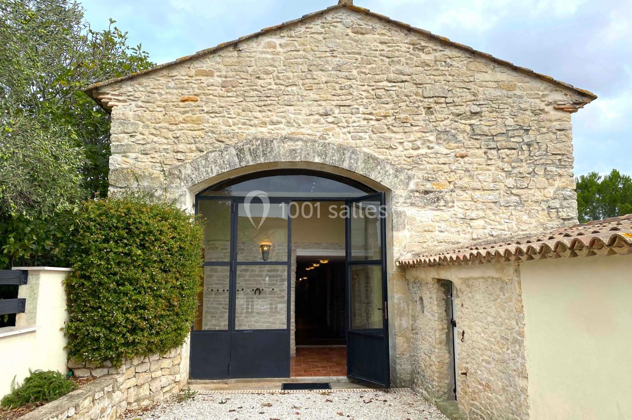 Façade en pierre d'un bâtiment ancien avec une grande porte vitrée et un chemin gravillonné devant.