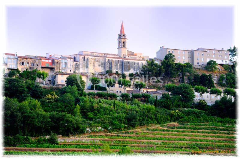 Village perché avec église au clocher pointu, entouré de maisons et de végétation, surplombant des vignes en terrasses.