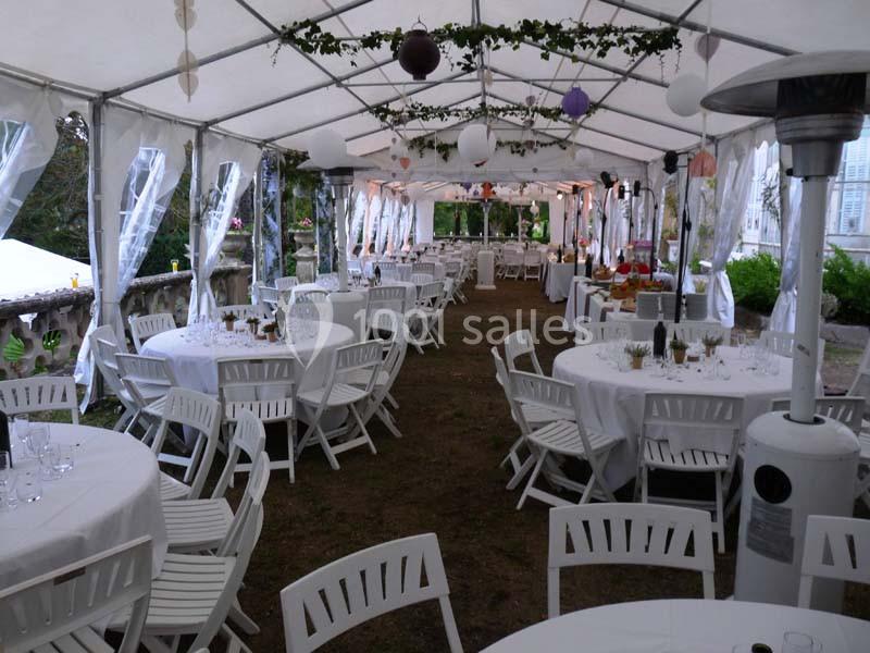 Intérieur d'une tente de réception avec des tables rondes dressées, des chaises blanches et des décorations suspendues.