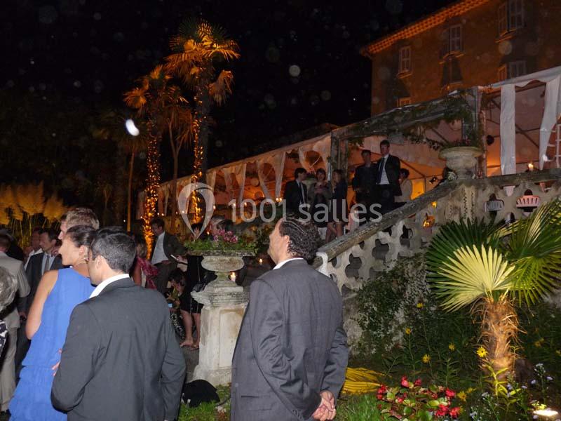 Groupe de personnes en tenue de soirée discutant devant un bâtiment éclairé et entouré de végétation, de nuit.