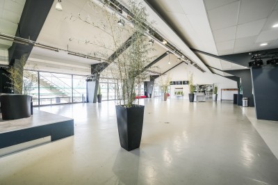 Salle avec grandes baies vitrées donnant sur une piste extérieure, aménagée avec tables, chaises et fauteuils rouges.