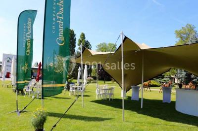 Salle avec grandes baies vitrées donnant sur une piste extérieure, aménagée avec tables, chaises et fauteuils rouges.