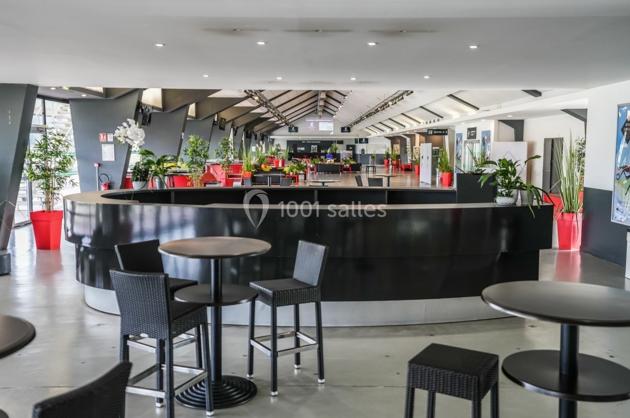 Espace intérieur lumineux avec comptoir noir central, tables hautes et plantes décoratives.