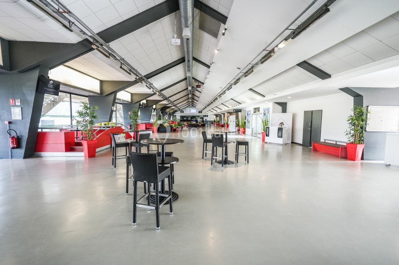 Vue d'un espace intérieur spacieux avec des tables, des chaises, des plantes et des zones d'assise rouges.