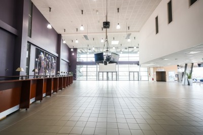 Salle avec grandes baies vitrées donnant sur une piste extérieure, aménagée avec tables, chaises et fauteuils rouges.