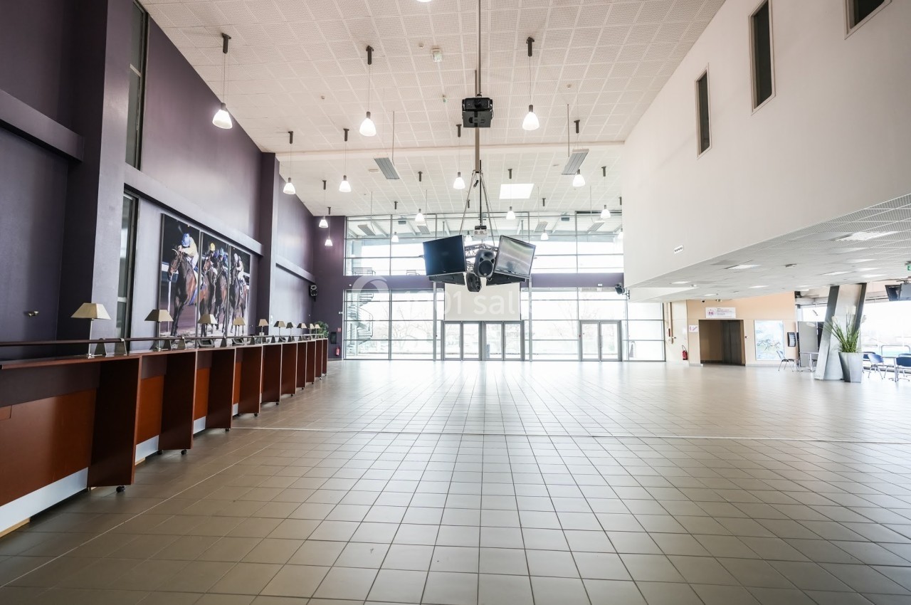 Vue intérieure d'un grand hall lumineux avec comptoirs à gauche, carrelage au sol et baies vitrées en fond.