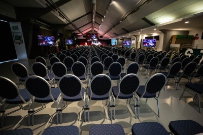 Salle avec grandes baies vitrées donnant sur une piste extérieure, aménagée avec tables, chaises et fauteuils rouges.