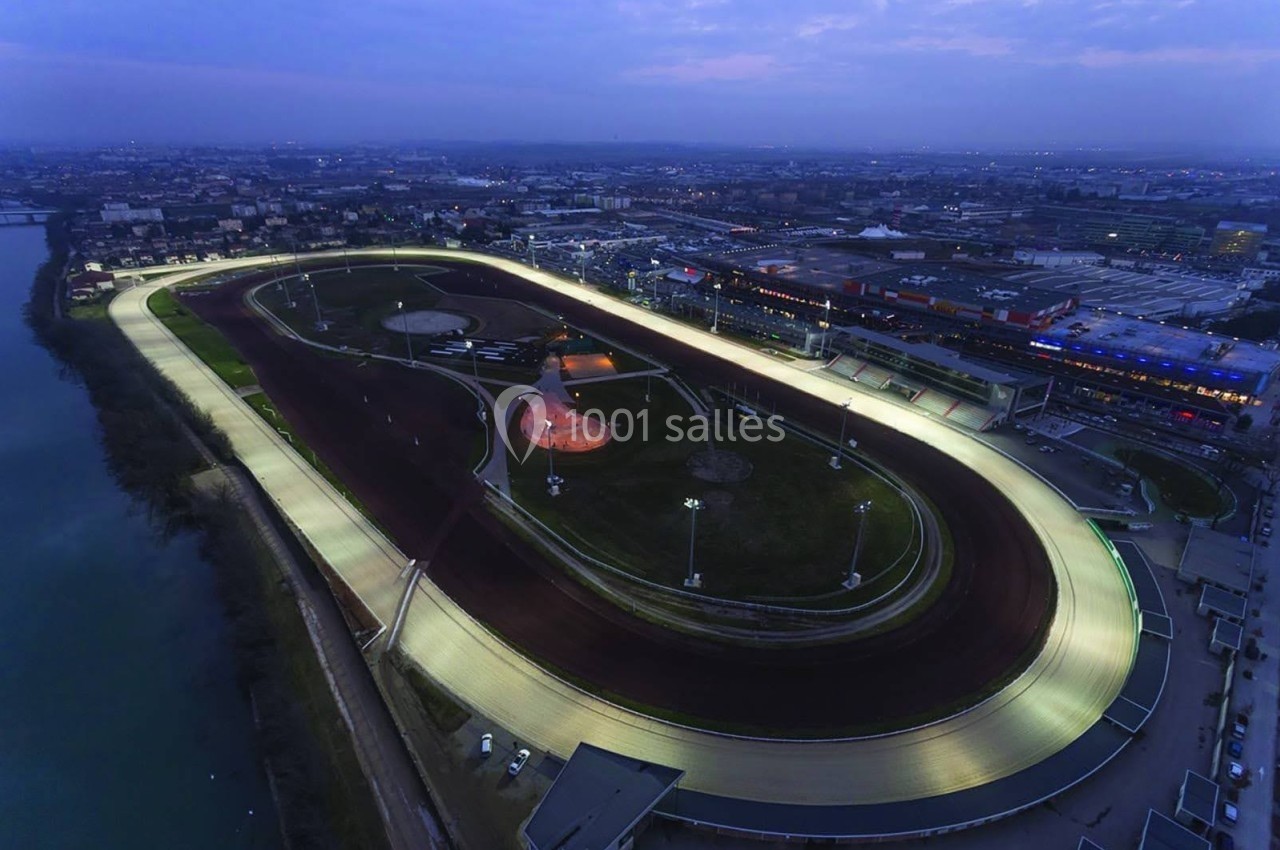 Vue aérienne d'un hippodrome éclairé de nuit, entouré de bâtiments et d'un cours d'eau.