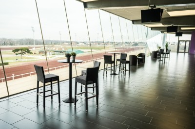 Salle avec grandes baies vitrées donnant sur une piste extérieure, aménagée avec tables, chaises et fauteuils rouges.