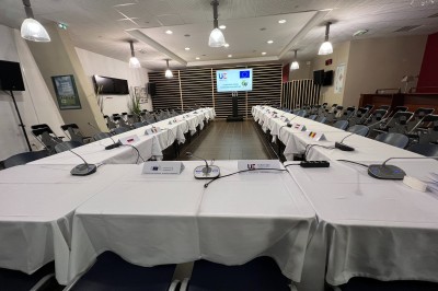 Salle avec grandes baies vitrées donnant sur une piste extérieure, aménagée avec tables, chaises et fauteuils rouges.