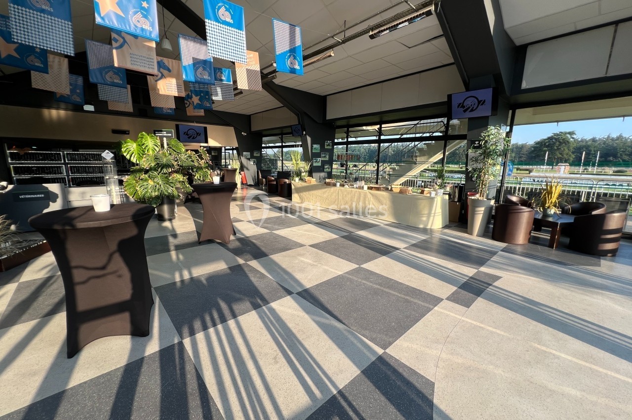 Salle lumineuse avec tables hautes noires, plantes et vue sur un espace extérieur ensoleillé à travers des baies vitrées.