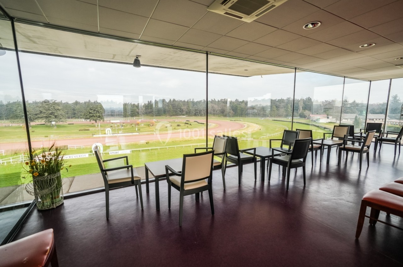 Salle avec des chaises alignées devant une baie vitrée offrant une vue sur une piste de course extérieure.