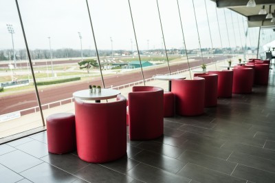 Salle avec grandes baies vitrées donnant sur une piste extérieure, aménagée avec tables, chaises et fauteuils rouges.
