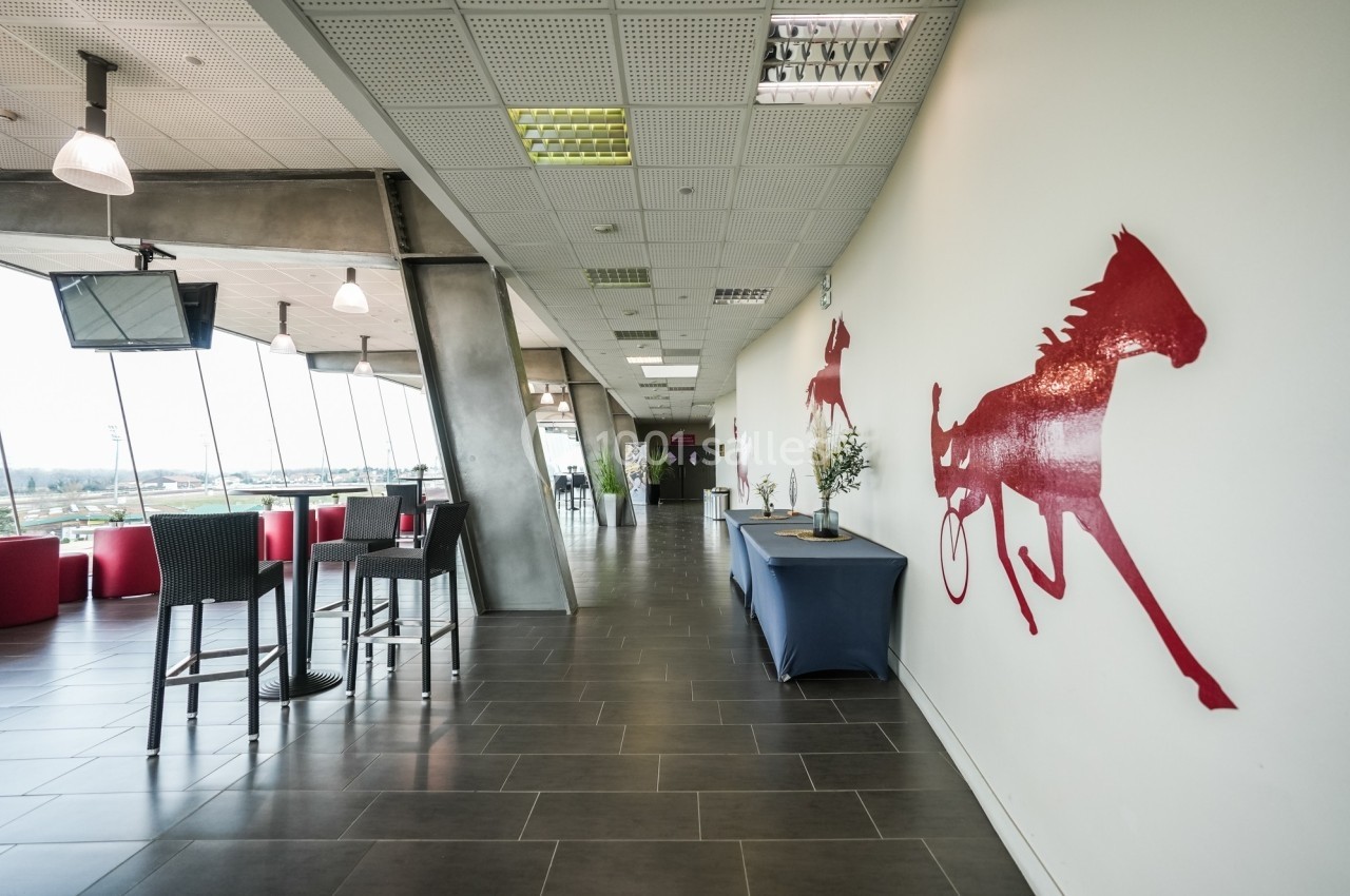 Salle lumineuse avec des décorations murales de chevaux rouges, des tables hautes et une vue sur l'extérieur.