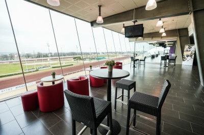 Salle avec grandes baies vitrées donnant sur une piste extérieure, aménagée avec tables, chaises et fauteuils rouges.