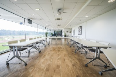 Salle avec grandes baies vitrées donnant sur une piste extérieure, aménagée avec tables, chaises et fauteuils rouges.