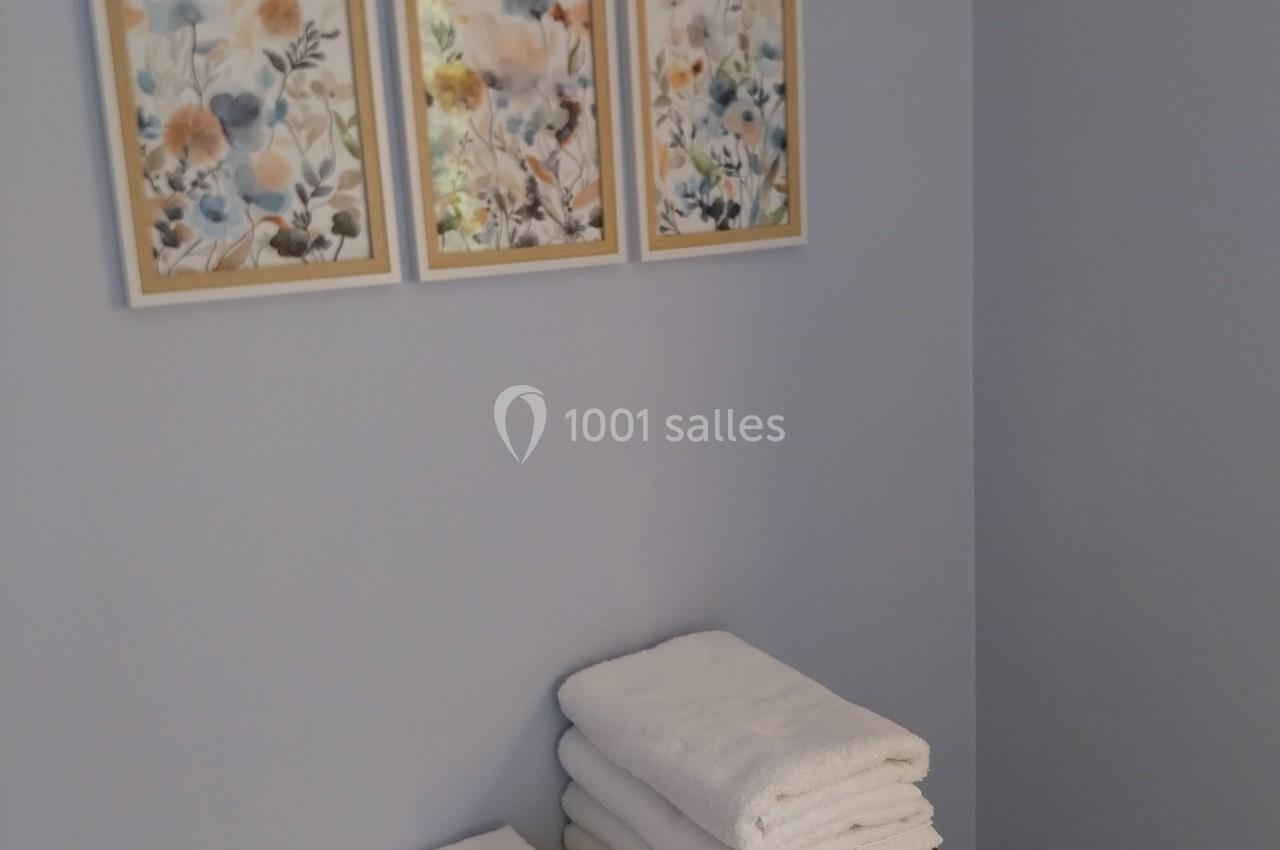 Table étroite avec des serviettes blanches pliées, une petite étiquette noire et trois cadres floraux accrochés au mur.