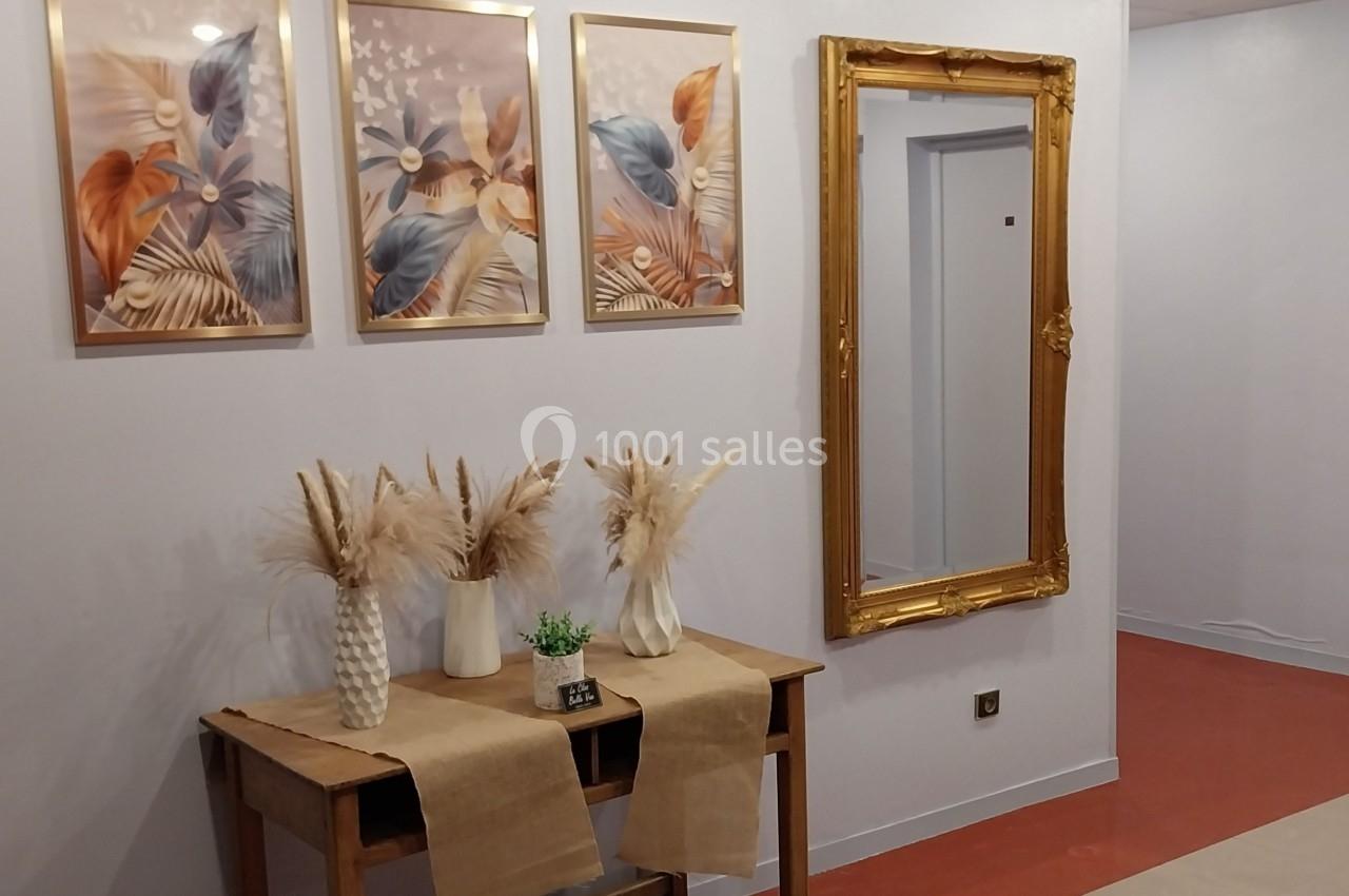 Table en bois décorée de vases avec des fleurs séchées, miroir doré et tableaux floraux accrochés au mur.