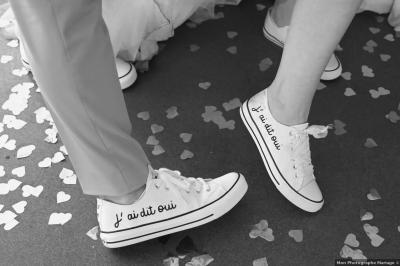 Deux personnes portant des baskets blanches avec l'inscription ’J'ai dit oui’, entourées de confettis en forme de cœur.