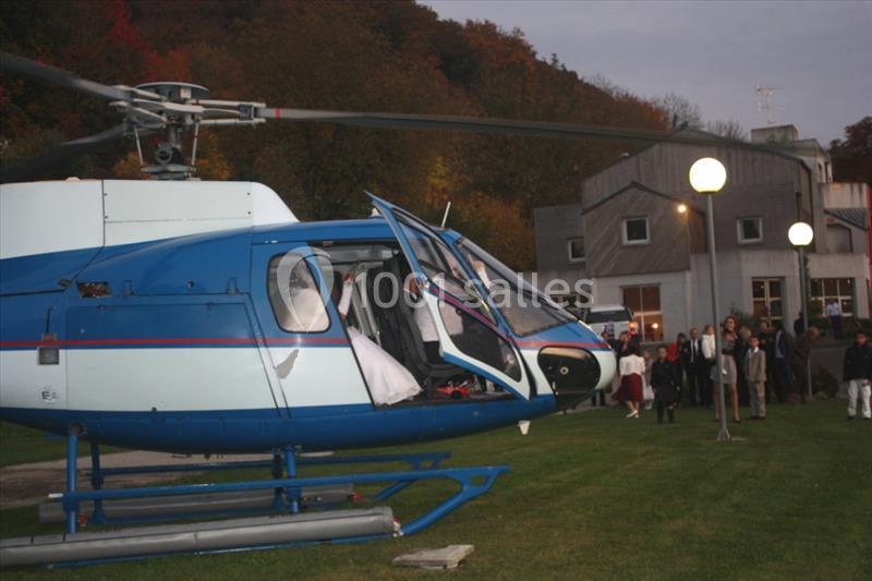 Hélicoptère bleu et blanc posé sur une pelouse près d'un bâtiment, avec des personnes rassemblées à proximité.