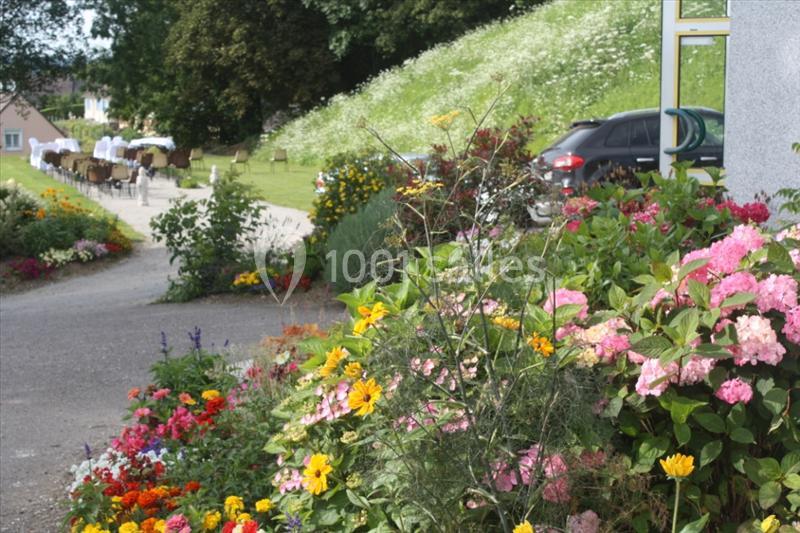 Massif de fleurs colorées bordant un chemin menant à une terrasse extérieure avec tables dressées.