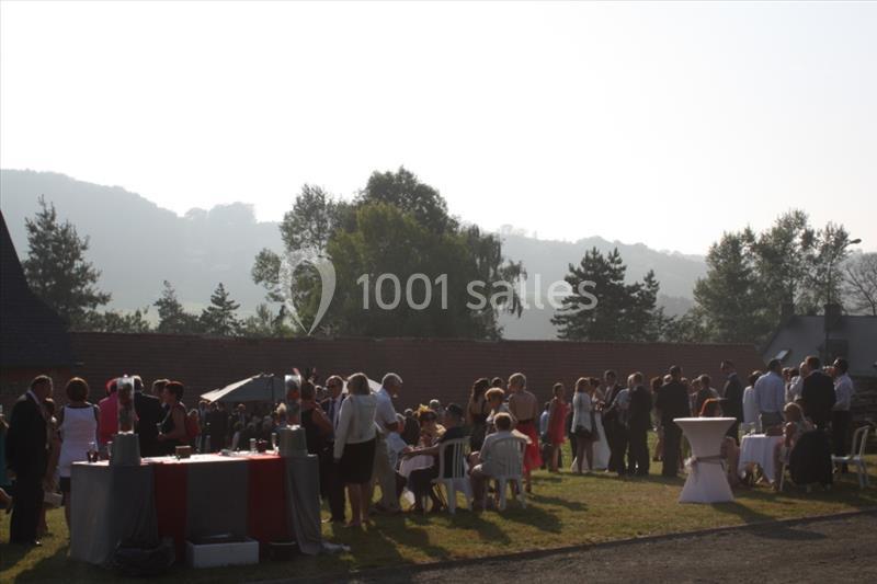 Groupe de personnes rassemblées en extérieur lors d'un événement, avec des tables et un paysage boisé en arrière-plan.