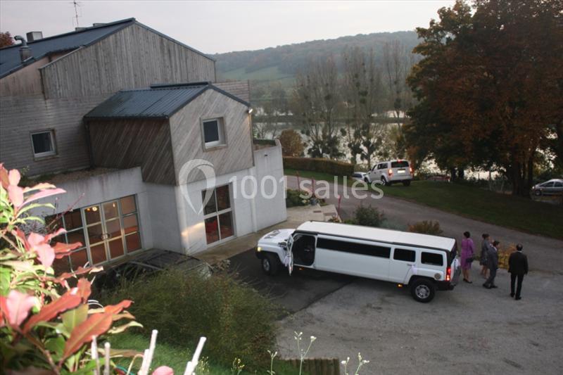 Une limousine blanche garée devant un bâtiment moderne en bois, entouré de végétation et d'un paysage rural.