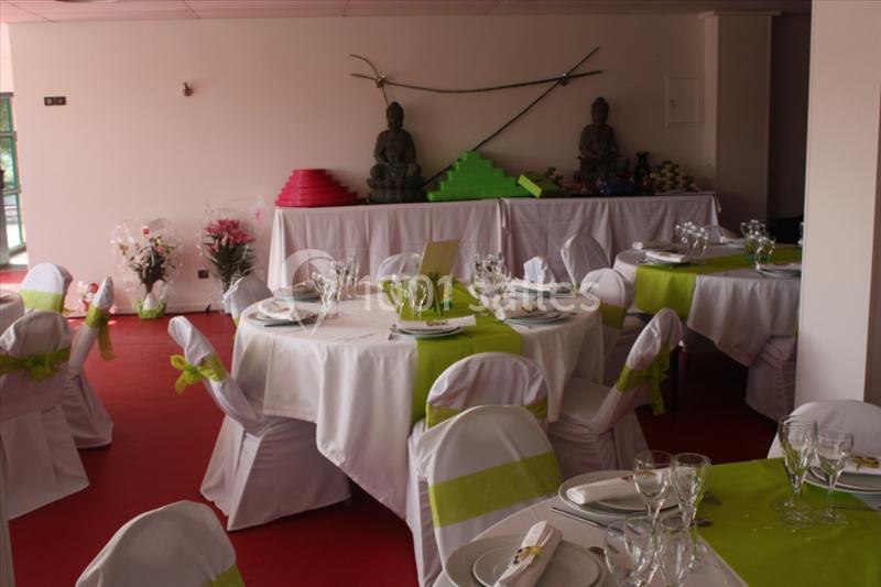 Salle décorée pour un événement avec tables rondes dressées, nappes blanches et accents verts, statues en arrière-plan.