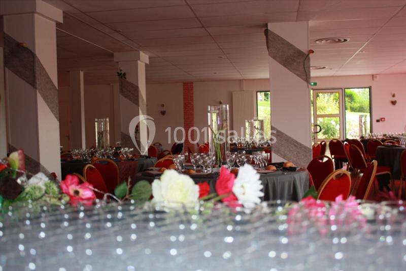 Salle de réception décorée avec des tables dressées, des chaises rouges et des fleurs en premier plan.