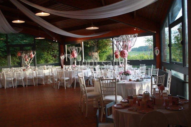 Salle de réception décorée avec des tables rondes, nappes blanches, chaises élégantes et ornements roses.