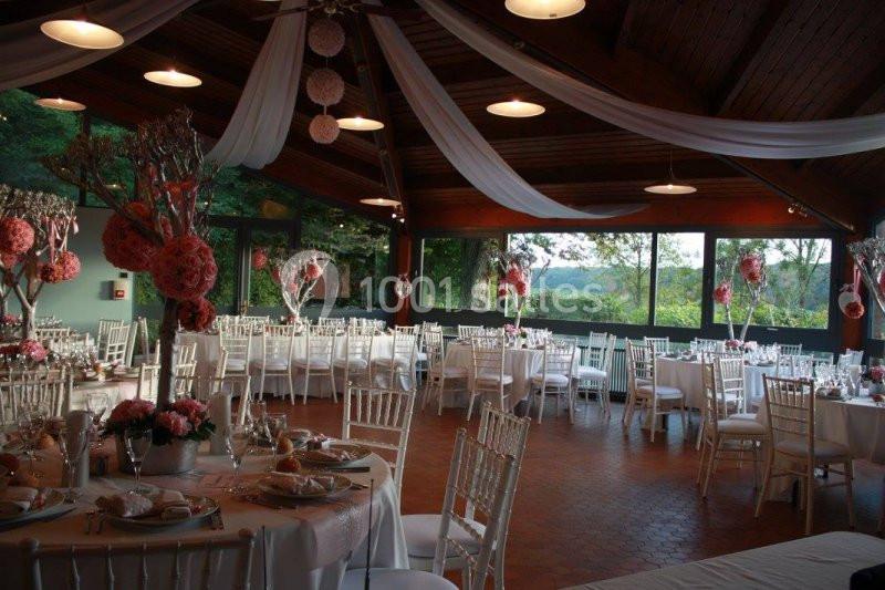 Salle de réception décorée avec des tables rondes, nappes blanches, chaises en bois clair et ornements floraux roses.