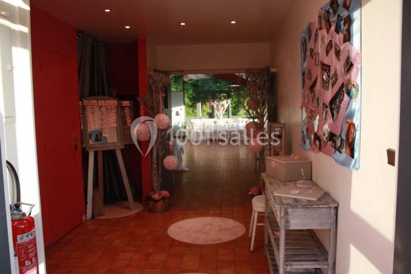 Entrée décorée avec des photos, des lanternes et un tableau, menant à une salle lumineuse aménagée pour un événement.